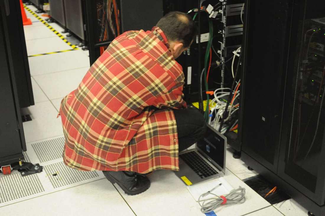 Technician kneeling at a live Linux server rack with a laptop, the hands-on patching work this cybersecurity news advisory demands from server infrastructure teams